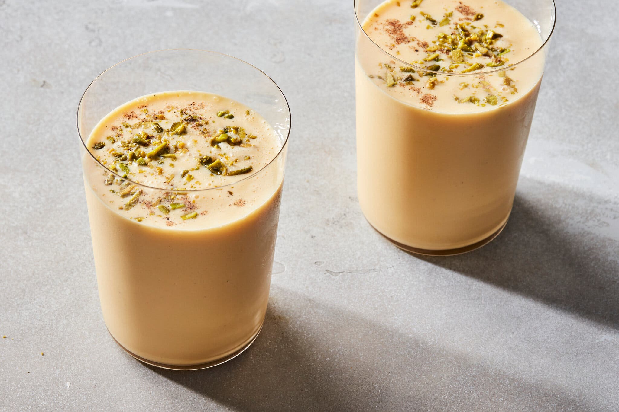 A side image of two cups filled with mango lassi and scattered with pistachios.