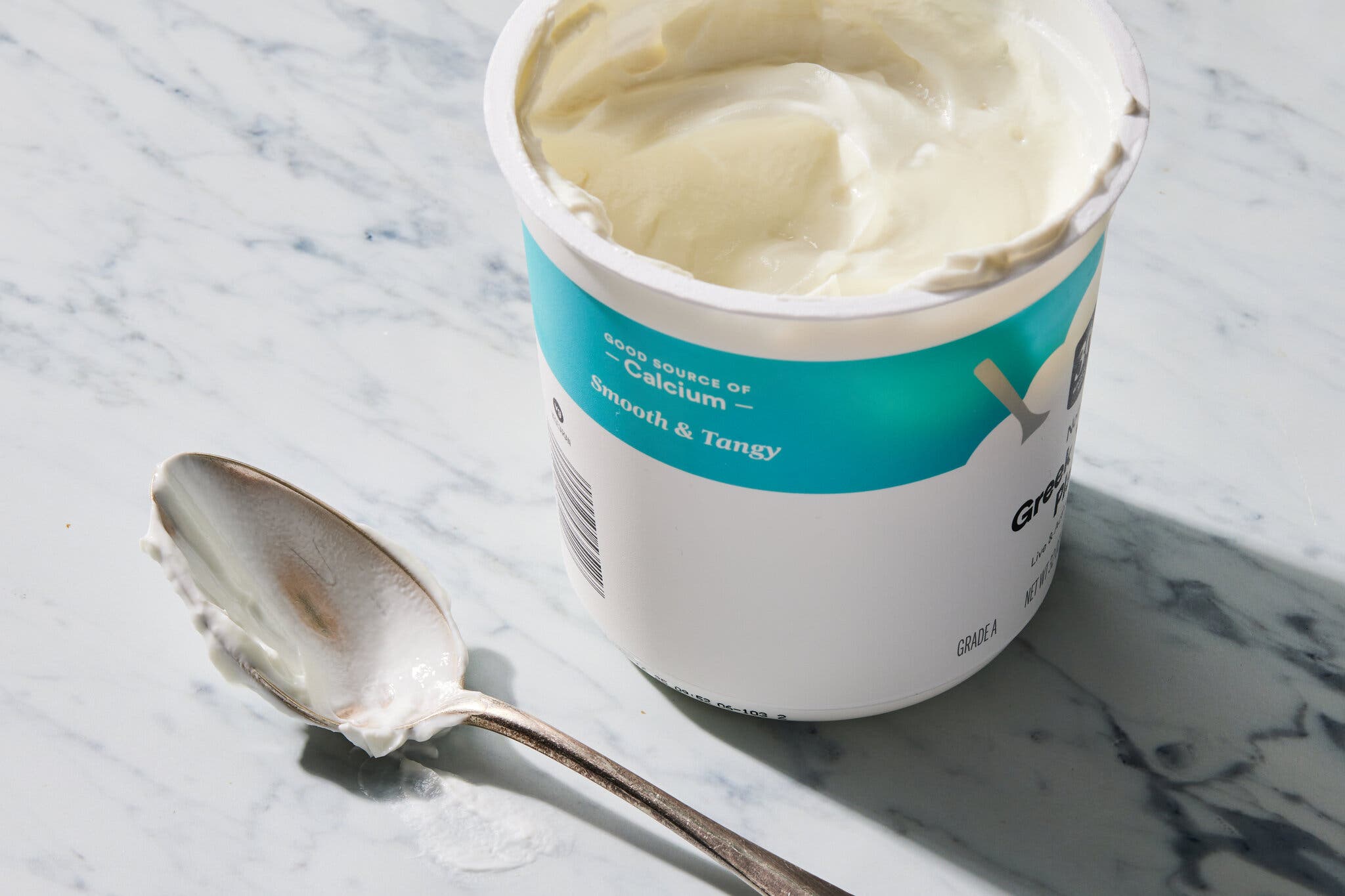 An image of an open tub of yogurt with a spoon next to it.