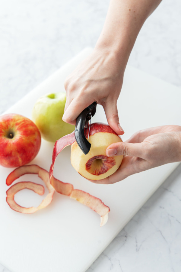 Peeling an apple with a vegetable peeler, two more apples waiting to be peeled on the side.