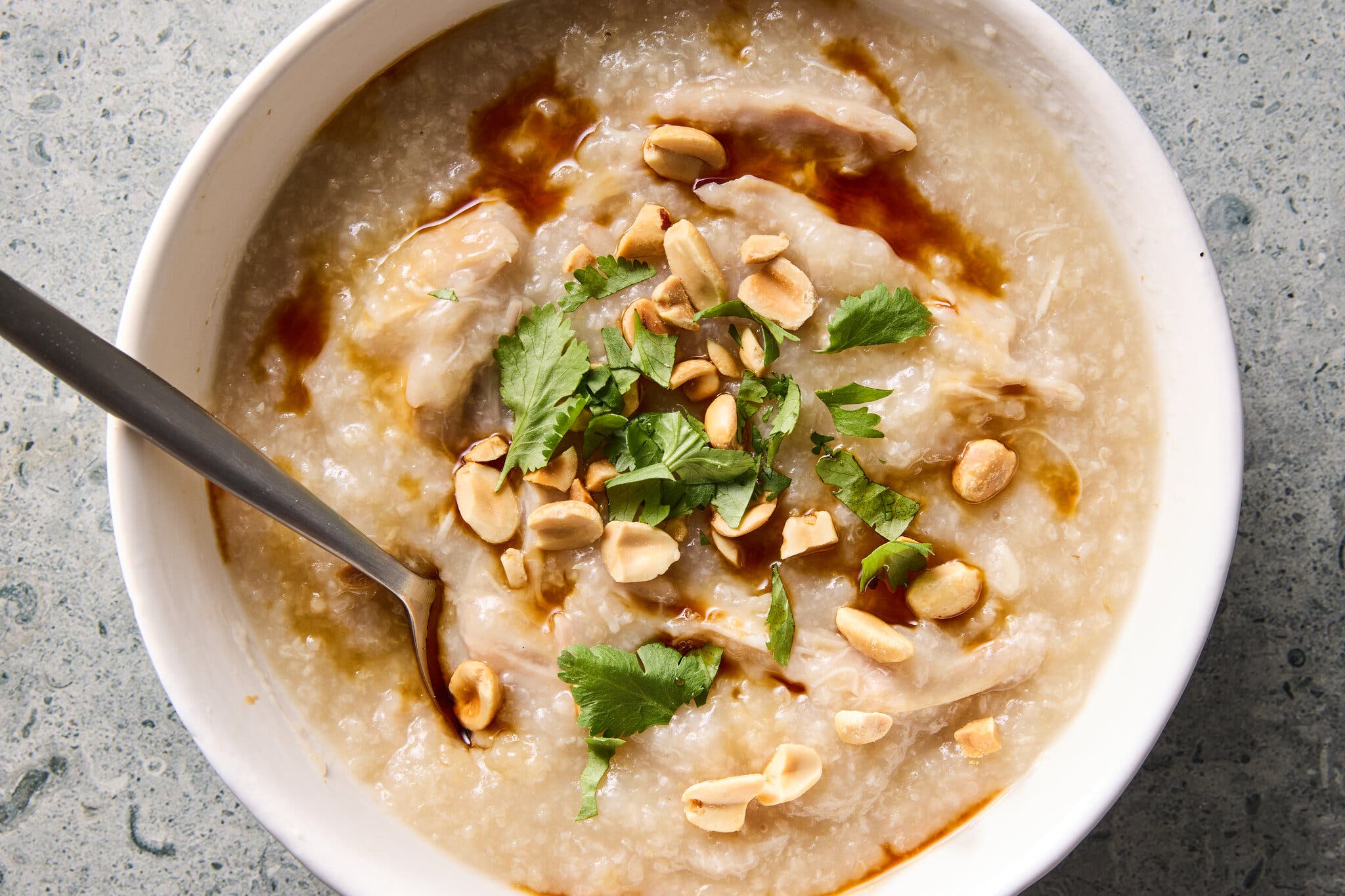An overhead shot of a bowl of congee with shredded chicken, garnished with peanuts, cilantro and a drizzle of soy sauce.