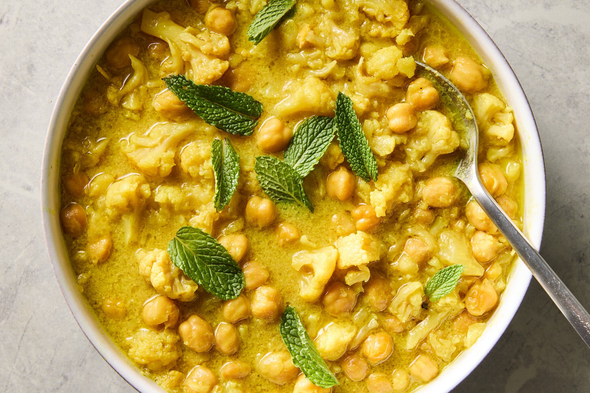 An overhead shot of a bowl of yellow chickpea and cauliflower curry, garnished with mint leaves.
