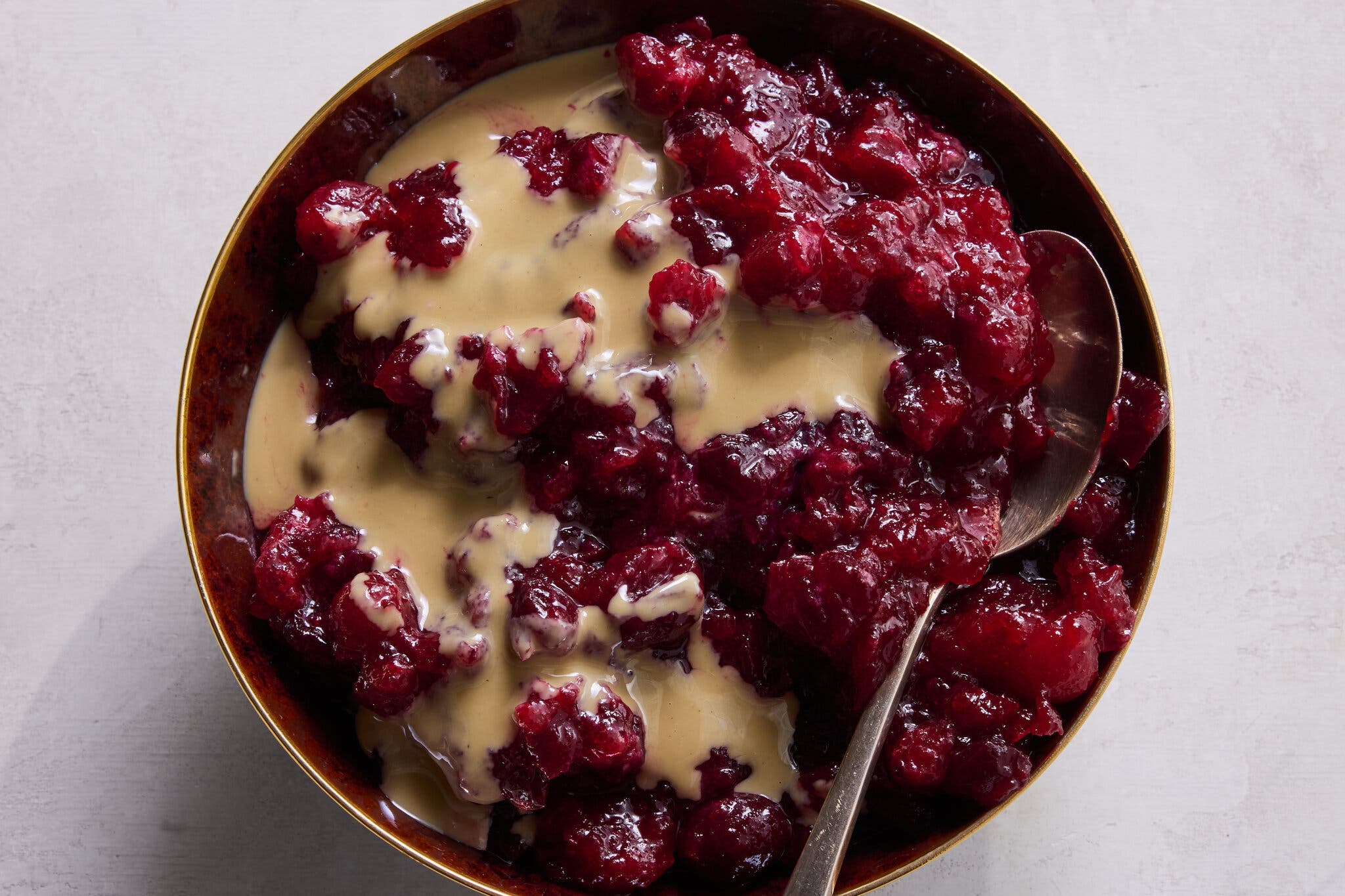 A close-up of chunky, dark red cranberry sauce drizzled with a tan sauce, served in a dark bowl.
