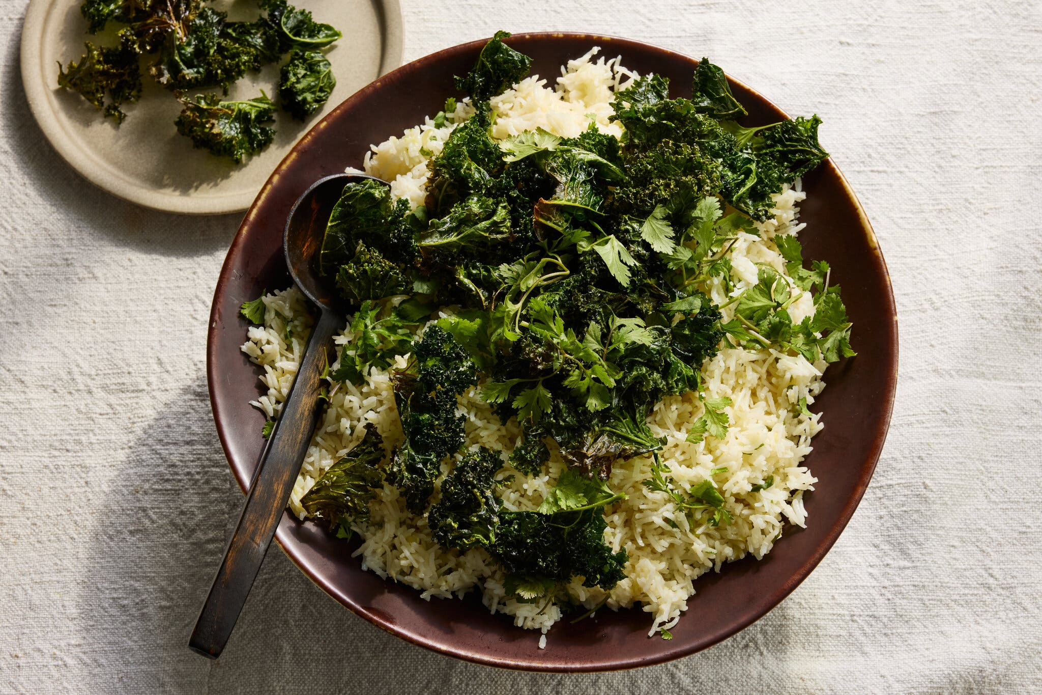A brown plate holds a large serving of fluffy coconut rice topped with bright green crispy kale and fresh cilantro.