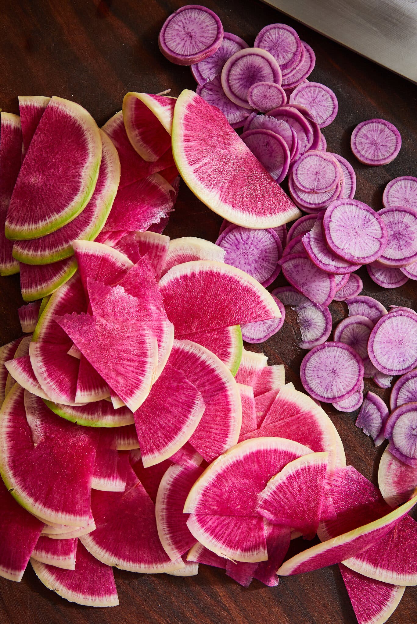 Pink and purple sliced radishes on a cutting board.