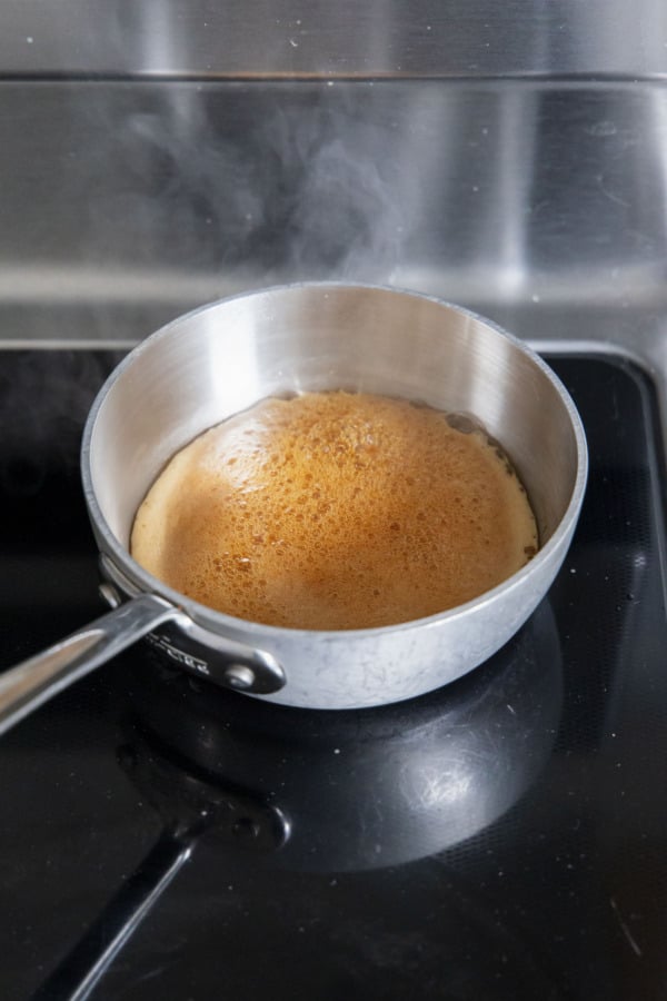Maple syrup bubbling vigorously in a small saucepan on the stove.
