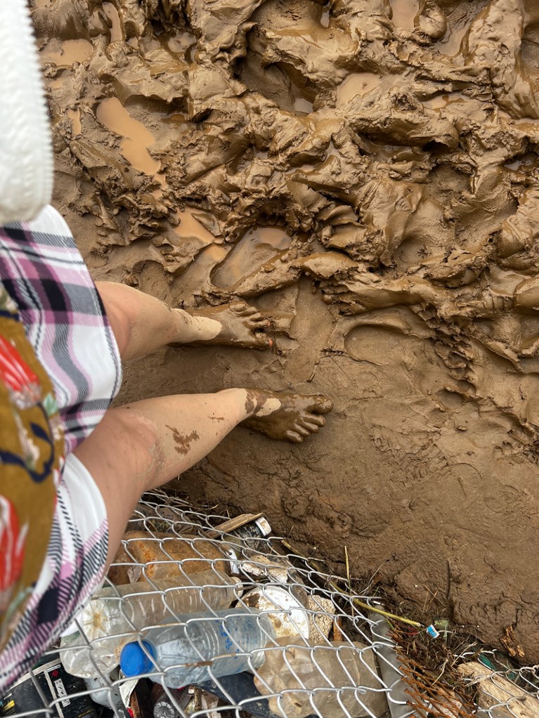 Bare feet standing in thick mud next to a chainlink fence