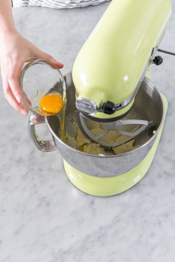 Adding an egg to mixing bowl with creamed butter and sugar.