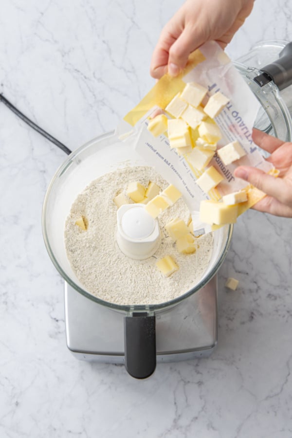Adding cubes of chilled butter to dry ingredients in food processor.